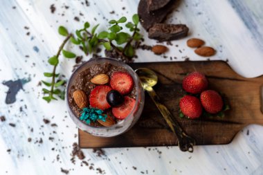 Çikolatalı puding, chia, çikolata ve çilek mavi bir masada.