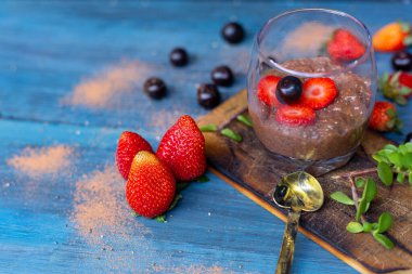 Çikolatalı puding, chia, çikolata ve çilek mavi bir masada.