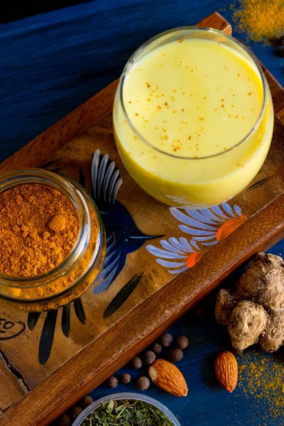 Golden milk powder and a glass with golden milk, on a blue table.