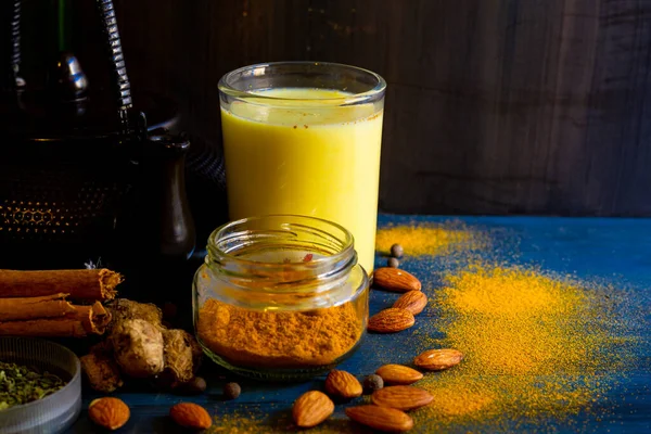 Golden milk powder and a glass with golden milk, on a blue table.