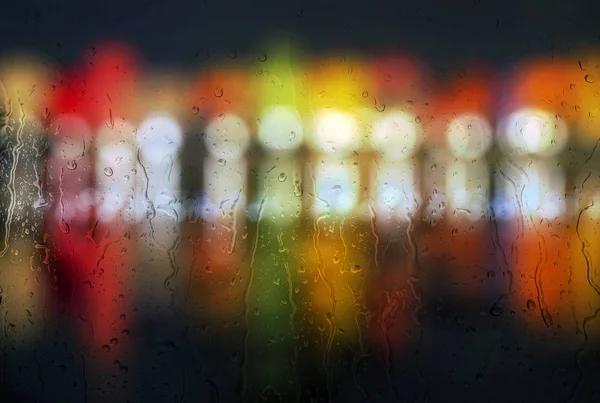 Gocce di pioggia sulla finestra di vetro con colorato di luce notturna all'esterno . — Foto Stock