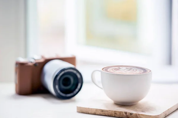 Tasse de café latte et caméra classique sur table blanche — Photo