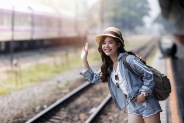 Gülümseyen ve tren istasyonu platformu, yaz tatil seyahat veya genç turist kavramı el sallayarak Asya sırt çantası gezgin kadın