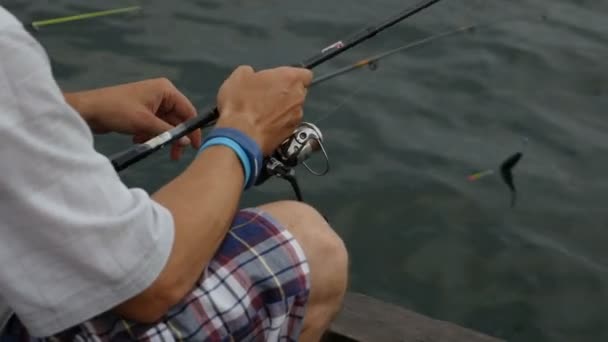 男と子供漁師は海のそばのパラペットに座って釣竿で魚を捕る — ストック動画