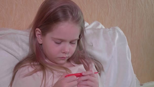 Symptoms of fever and coronavirus, a girl measures body temperature. Upset girl looks at a digital thermometer in her hand, the concept of the common cold and flu — Stock Video