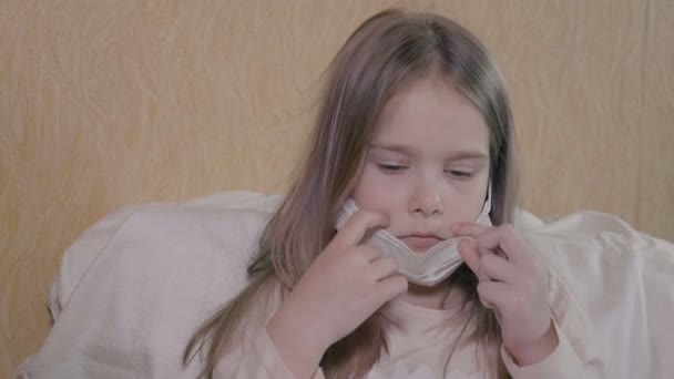 La fille a un mal de tête sévère et de la fièvre. La fille a le coronavirus ncov-19. La fille porte un masque médical, l'auto-isolement . — Video