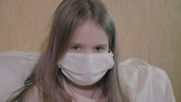 Het meisje heeft ernstige hoofdpijn en koorts. Het meisje heeft ncov-19 coronavirus. Het meisje draagt een medisch masker, zelf-isolatie. — Stockvideo