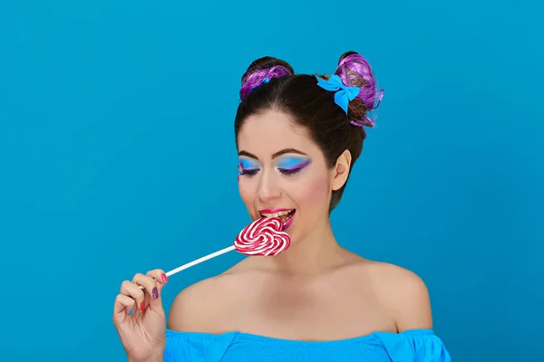 Pretty woman with bows in her hair and blue eyes with red and white lollipop on blue background