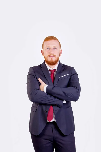 Kızıl saçlı işadamı kollarını kavuşturdu. Kırmızı takım elbise ve kravat takıyor.
