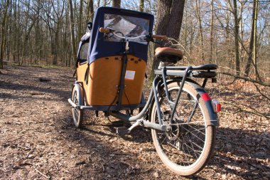 Doğada bataryası olan E-Kargo bisikleti. Berlin 'de bir ormanda çadır parkı olan tahta kargo bisikleti. Arkaplan bulanık.