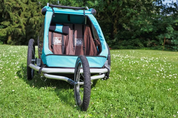 Empty bicycle trailer with front wheel in a park. Vehicle to transport children on a green meadow.