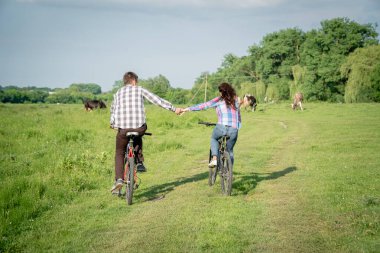 Yeşil çimlerde bisiklet süren bir kızla bir adam.