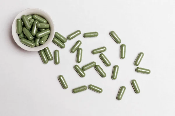 Capsules with powder of dried medicinal plants are scattered on a white background.