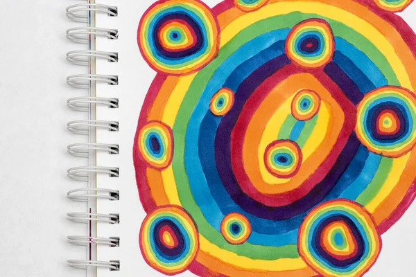 Children\'s drawing with markers in a drawing album with springs: a bright fantasy rainbow in the form of circles. Illustration of joy and good mood.