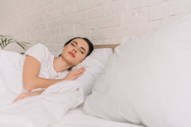 selective focus of beautiful woman sleeping on white bedding clipart