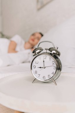selective focus of vintage alarm clock on white bedside table and sleeping girl on background clipart