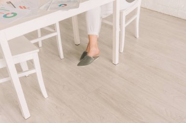 Pijama ve terlik giyen serbest çalışanın grafikler ve çizelgelerle masa başında çalışmasının kesilip atılmış görüntüsü.
