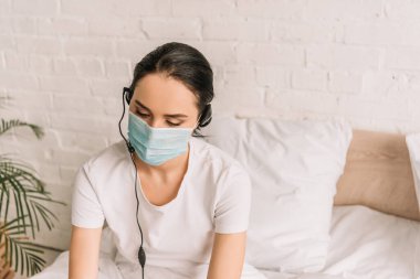 Evde çalışan kulaklık ve tıbbi maske takan ciddi bir uzaktan kumanda operatörü.
