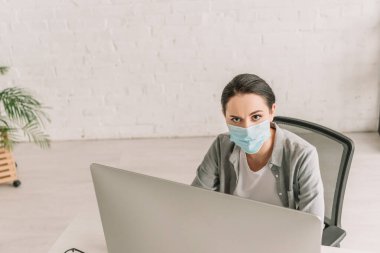 Medikal maskeli serbest çalışanın evde çalışırken kameraya baktığı yüksek açılı görüntü