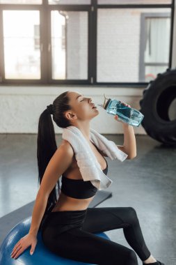 Havlu ve gözleri kapalı, su içen ve spor salonunda spor salonunda oturan güzel bir sporcu.