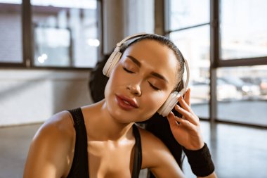 Spor salonundaki kulaklıkla müzik dinleyen kapalı gözlü kadın portresi.
