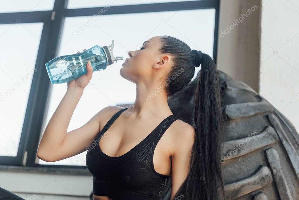 Sexy sportswoman drinking water near tire in sports center