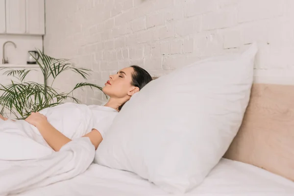 Selektiver Fokus der schönen brünetten Frau, die auf weißer Bettwäsche schläft — Stockfoto
