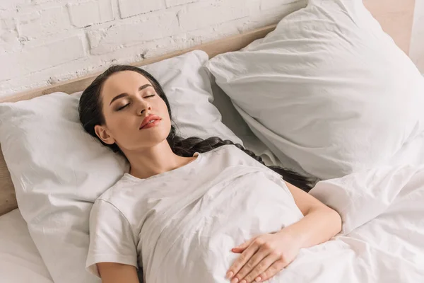 Hochwinkelaufnahme der schönen brünetten Frau, die auf weißem Bettzeug schläft — Stockfoto