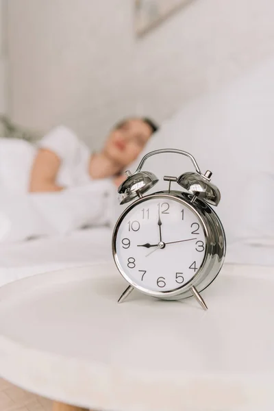 Selektiver Fokus des Vintage-Weckers auf weißem Nachttisch und schlafendem Mädchen im Hintergrund — Stockfoto