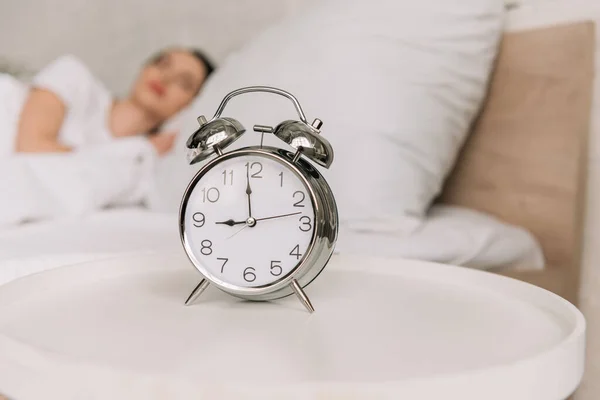 Selective focus of vintage alarm clock on bedside table and sleeping woman on background — Stock Photo