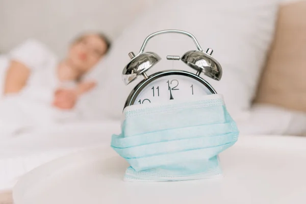 Selective focus of vintage alarm clock wrapped in medical mask and sleeping woman on background — Stock Photo