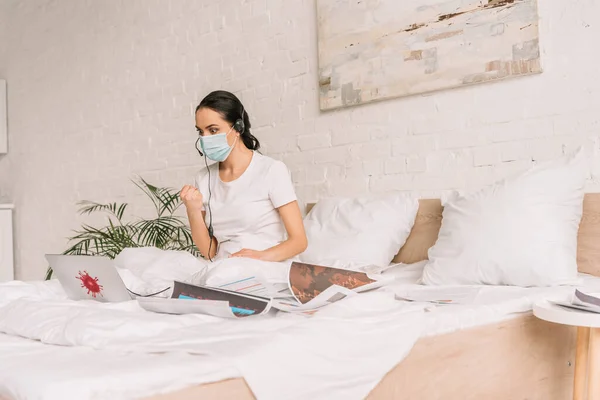 Angry remote operator in medical mask and headset working in bed and showing fist while having video call — Stock Photo