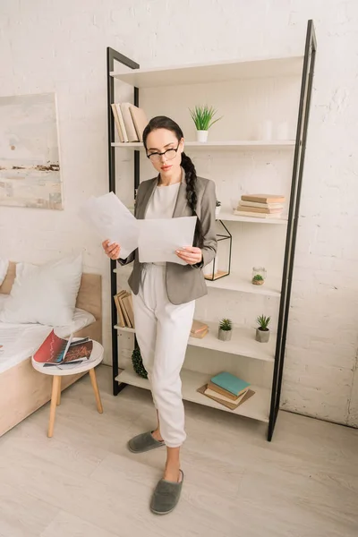 Femme d'affaires sérieuse en blazer sur pyjama regardant la caméra tout en se tenant dans la chambre — Photo de stock