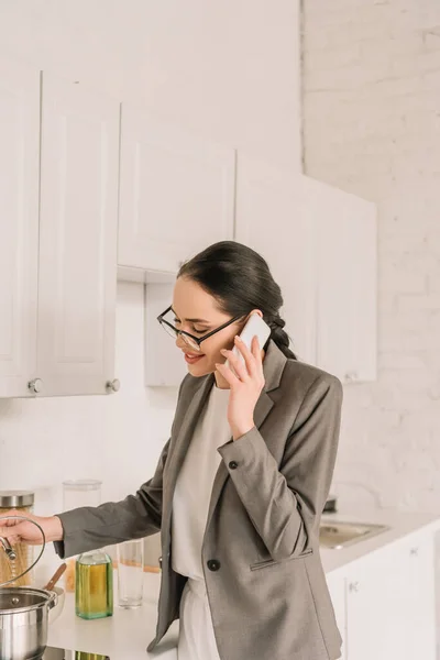 Lächelnde Geschäftsfrau im Blazer über Pyjama beim Kochen und Telefonieren in der Küche — Stockfoto