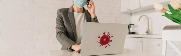 Abgeschnittene Ansicht einer Geschäftsfrau in medizinischer Maske, die auf einem Smartphone in der Nähe eines Laptops mit einem Aufkleber für Coronavirus-Bakterien spricht, horizontales Bild — Stockfoto