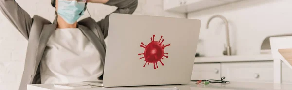 Panoramaaufnahme einer Geschäftsfrau mit medizinischer Maske, die in der Küche in der Nähe ihres Laptops sitzt und einen Aufkleber mit Coronavirus-Bakterien trägt — Stockfoto