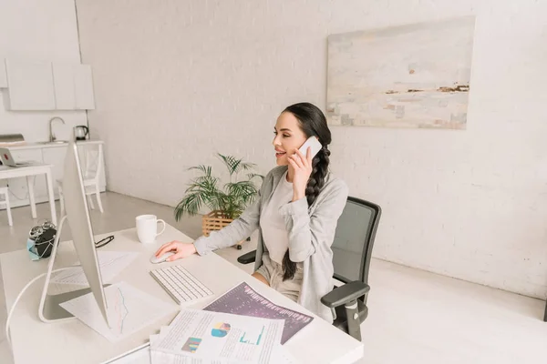 Junge Freiberuflerin spricht auf Smartphone, während sie am Computer in der Nähe von Dokumenten und Wecker in medizinische Maske gehüllt arbeitet — Stockfoto