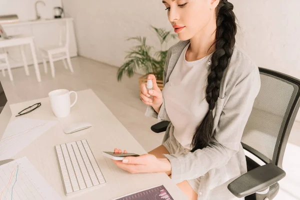 Attractive freelancer spraying sanitizer on eyeglasses while working at home — Stock Photo