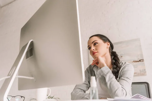 Foyer sélectif de pigiste réfléchi regardant le moniteur d'ordinateur près de la bouteille de pulvérisation avec désinfectant — Photo de stock