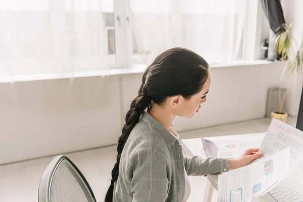 Pigiste attentif regardant des documents avec des infographies tout en travaillant à la maison — Photo de stock