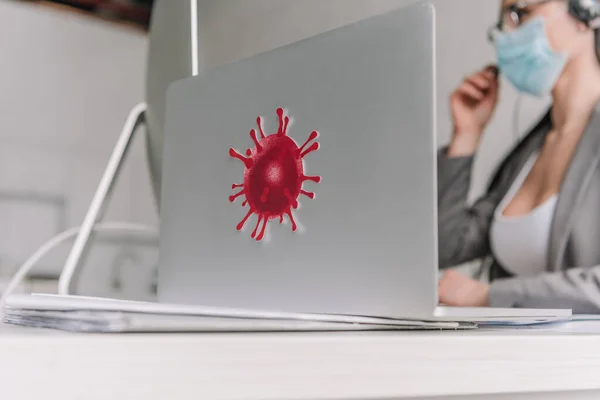 Selektiver Fokus des Laptops mit Coronavirus-Bakterien-Aufkleber in der Nähe einer Geschäftsfrau in medizinischer Maske, die zu Hause arbeitet — Stockfoto