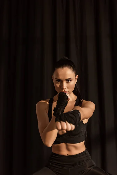 Attractive sportswoman in fighting position with outstretched hand looking at camera on black — Stock Photo