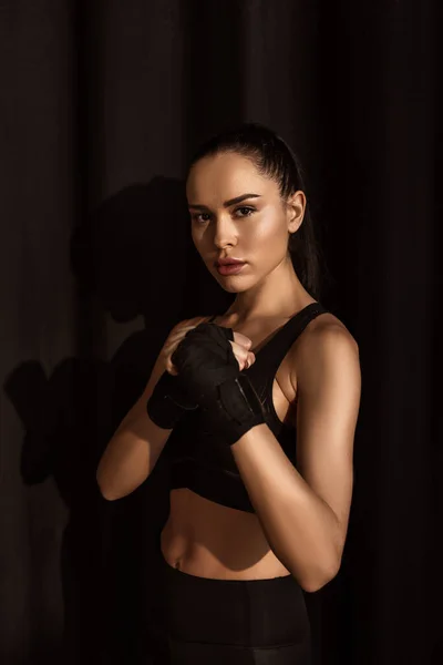 Attractive sportswoman in fighting position looking at camera on black — Stock Photo