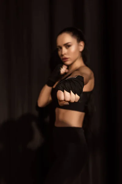 Selective focus of sportswoman in fighting position showing fist with outstretched hand and looking at camera on black — Stock Photo