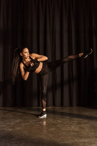 Attractive sportswoman kicking with leg on black background — Stock Photo