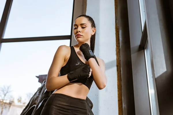 Vista de ángulo bajo de la deportista en guantes deportivos cerca de neumático en el gimnasio - foto de stock