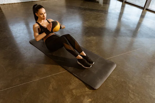 High angle view of sportswoman holding ball and doing abs on fitness mat in gym — Stock Photo