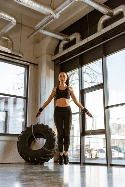 Sportswoman jumping with skipping rope and looking at camera in gym — Stock Photo