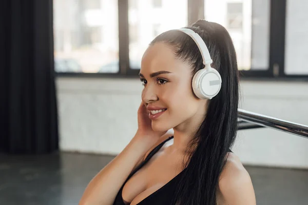 Сексуальная спортсменка улыбается и слушает музыку в наушниках в спортзале — стоковое фото