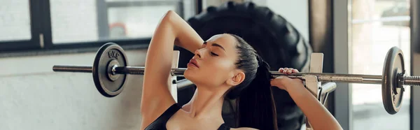Encabezado del sitio web de la deportista con los ojos cerrados cerca de la barra en el gimnasio - foto de stock